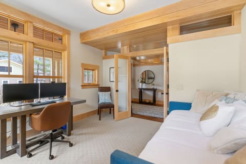 Cozy office space featuring a desk with dual monitors, a blue couch, and an inviting entryway.