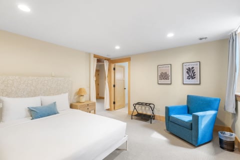 Cozy bedroom with white bed, blue armchair, and framed Matisse artworks.
