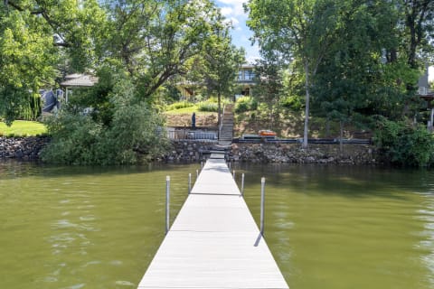 Wooden dock extending into a green lake with houses and trees in the background.