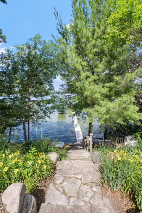 Stone pathway surrounded by flowers and trees leading to a calm lake.
