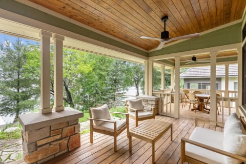 A well-furnished porch with wooden flooring, chairs, and a dining area amidst greenery.