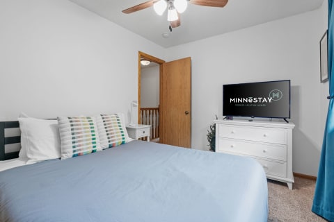 Cozy bedroom with light blue bedding and a television on the dresser.