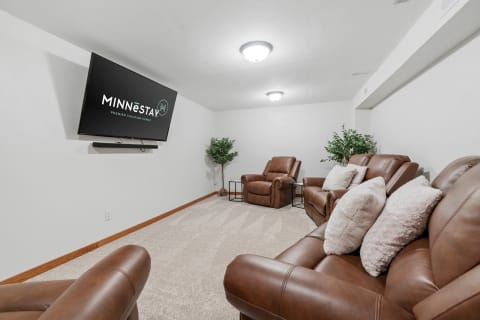 A room with brown recliners, a mounted TV displaying a logo, and plants in the corners.