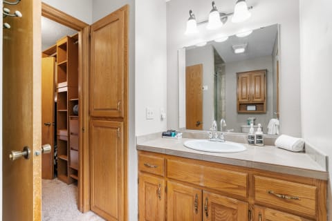 Interior of a cozy bathroom featuring wooden cabinetry, a sink, large mirror, and storage space.