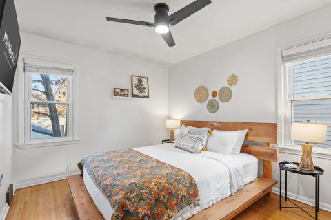 Warm wooden bedroom featuring a colorful quilt, woven decor, and a nightstand lamp.