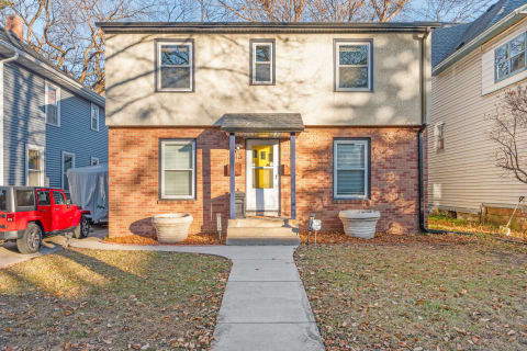 Exterior view of a two-story home with brick and stucco facade, featuring a front porch and a red Jeep parked nearby.