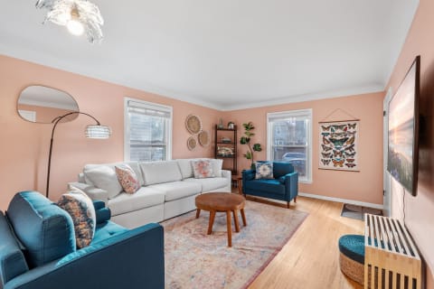 A living room with a white sectional sofa, blue armchair, wooden coffee table, and peach walls, illuminated by natural light.