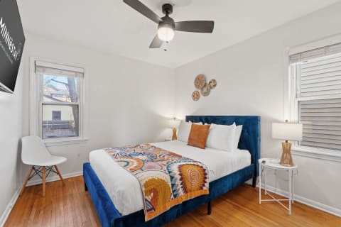 A bright bedroom featuring a blue upholstered bed, decorative throw blanket, and modern furnishings.