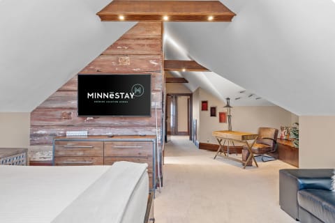 Cozy attic bedroom featuring a wooden wall, flat-screen TV, and stylish furnishings.