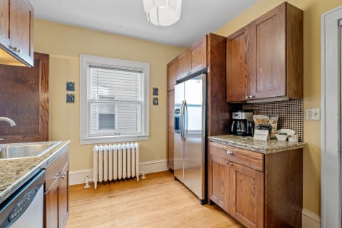 A charming kitchen featuring wooden cabinets, a stainless steel refrigerator, and a sunny atmosphere.