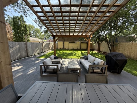 Outdoor patio beneath a wooden pergola with comfortable seating and a grill.