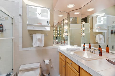 A contemporary bathroom featuring a glass shower, sink with amber soap bottles, mirror cabinet, and neatly hung towels.