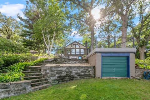 An outdoor view featuring a modern cabin with large windows, surrounded by trees and stone steps.