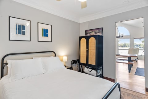A bedroom featuring a black metal bed, white bedding, framed posters, and a cozy cabinet.