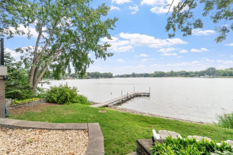 Lakeside view featuring a dock, trees, and a clear blue sky.