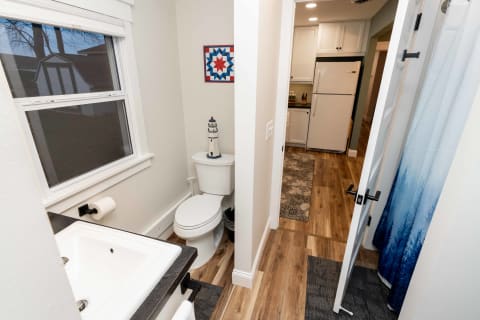 Compact bathroom with a toilet and sink, leading into a kitchen.