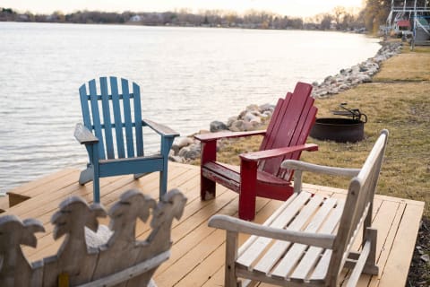 Three chairs on a wooden deck by the lake at sunset.