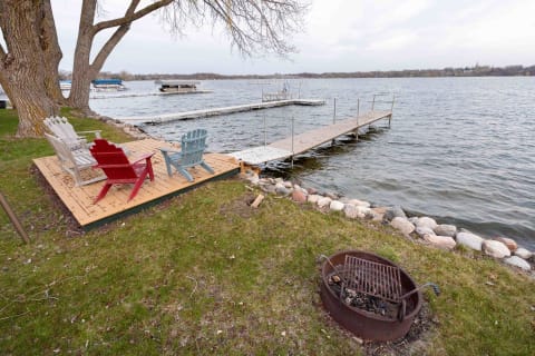 Lakeside view featuring colorful Adirondack chairs, a dock, and a fire pit.