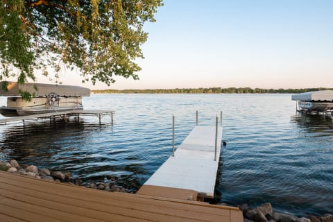Lakeside scene featuring a white dock, boats, and lush trees.