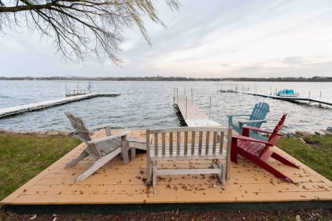 Lakeside scene with Adirondack chairs and a wooden dock under a twilight sky.