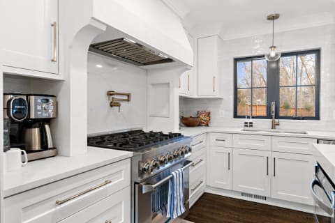 A bright and modern kitchen featuring white cabinetry, a stainless steel stove, and a large window.