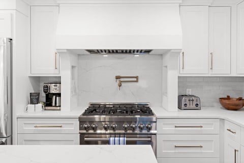 Modern kitchen with a stainless steel gas range, white cabinets, and marble backsplash.