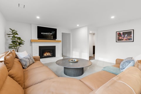 Contemporary living room featuring a brown leather sectional, a round coffee table, and a white brick fireplace with a mounted TV.