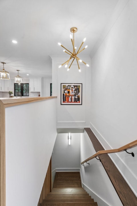 Modern staircase with chandelier and colorful painting, showcasing wood and white design.