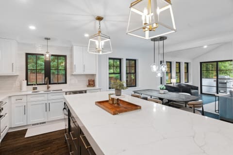 A contemporary kitchen featuring a large marble countertop, dark cabinetry, and a cozy dining area with a grey table and chairs.