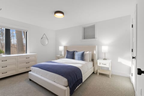 Modern bedroom featuring a white bed with blue accents, natural light, and minimalist decor.