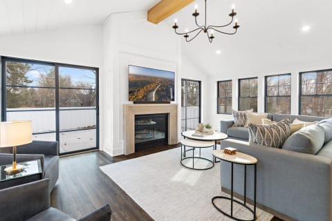 A modern living room with a sectional sofa, coffee tables, and large windows overlooking nature.