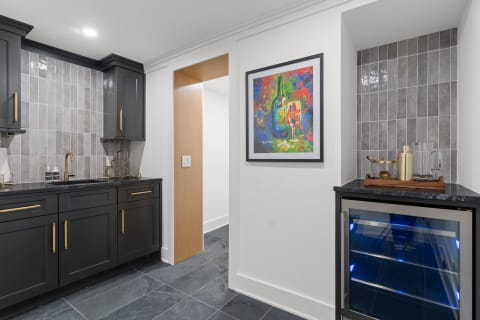 A stylish kitchenette with black cabinets, a colorful painting, and a wine cooler.