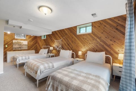A cozy bedroom featuring three beds with white linens and plaid blankets, complemented by wooden paneling and soft lighting.