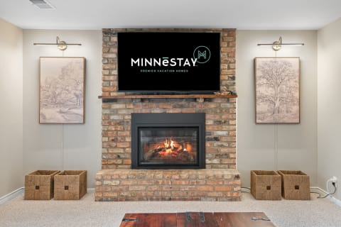 Living room with a brick fireplace, artwork, and a flat-screen TV displaying the MINNĒSTAY logo.