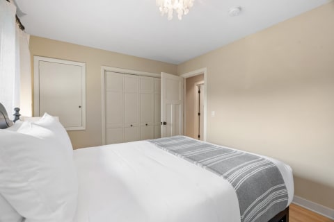 A tidy bedroom featuring a bed with white linens and a light gray throw blanket, adorned with curtains and a chandelier.