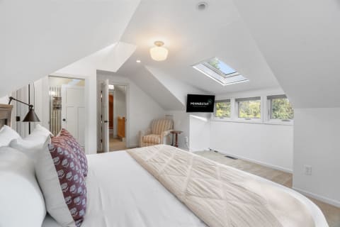 Bright and airy attic bedroom featuring a bed, armchair, and skylight.