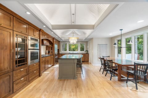 Interior of a modern kitchen with wooden cabinets, stainless steel appliances, and large windows.