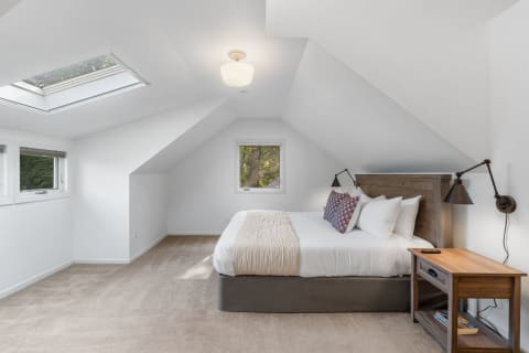 Bright attic bedroom with white walls, skylight, and a wooden bed frame.
