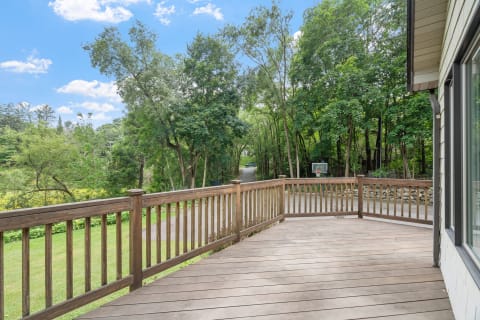 Wooden deck with a view of trees and a basketball hoop in the background.