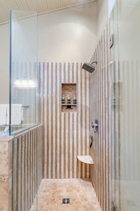 A contemporary shower featuring glass panels, beige tiled walls, and a built-in shelf with toiletries.