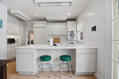 Your sleek white kitchen features modern appliances and a breakfast bar with vibrant green stools for casual meals.