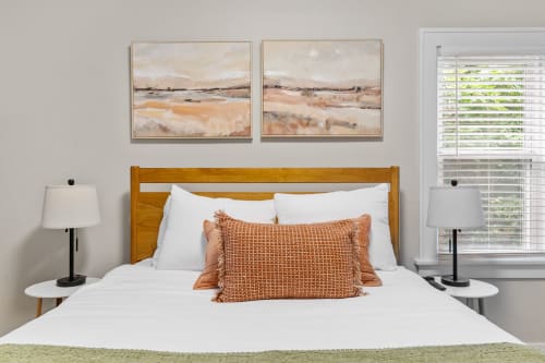 Sink into crisp white linens and warm wood tones in your peaceful bedroom retreat, where soft lighting and serene artwork create the perfect ambiance.