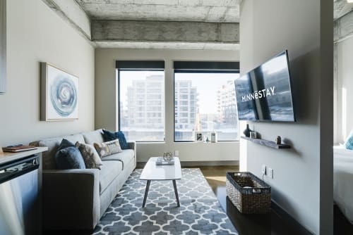 Unwind in your modern living space with exposed concrete ceilings, plush seating, and stunning city views through floor-to-ceiling windows.
