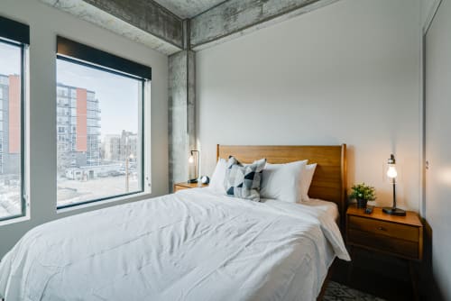 Drift off in your modern bedroom with crisp white linens, warm wood accents, and city views through expansive windows.