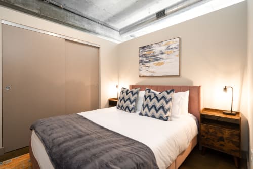Your chic bedroom features exposed concrete ceilings, plush bedding with geometric pillows, and modern furnishings that create an urban retreat.