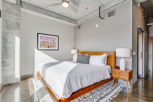 Unwind in your modern bedroom featuring exposed concrete beams, crisp linens, and warm wood furnishings that create the perfect urban retreat.
