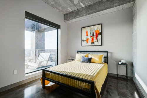 Rest peacefully in your modern bedroom featuring exposed concrete beams and floor-to-ceiling windows that frame the city beyond.