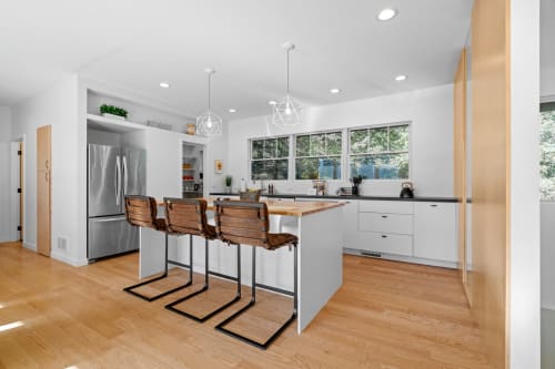 Your modern kitchen features sleek white cabinets, stainless steel appliances, and warm wood accents with garden views through large windows.